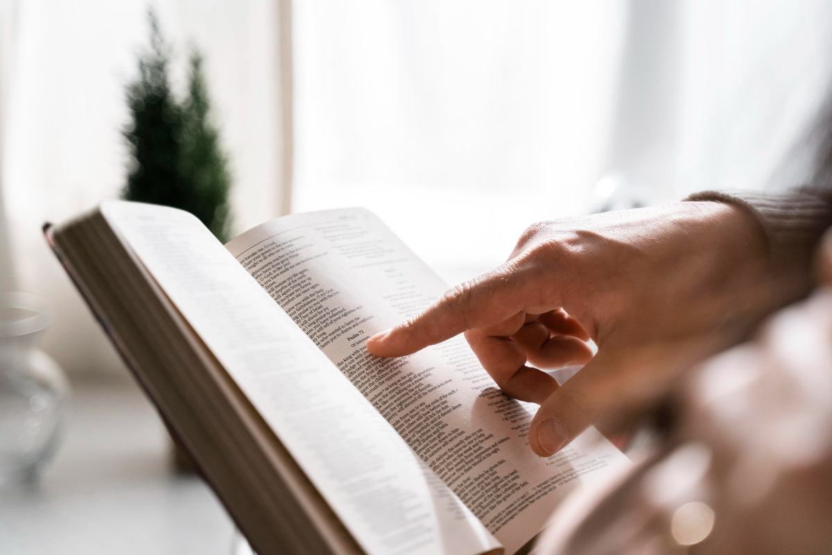 teologia-EAD-grade-curricular-mercado-de-trabalho-e-salarios-Imagem enquadra uma mão branca apontando pra um trecho de texto em um livro aberto. 