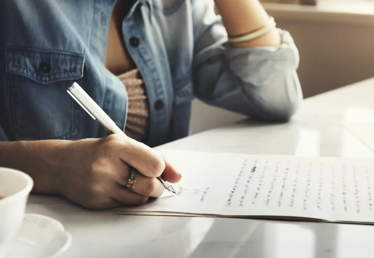 Como fazer uma redação para o Encceja Ensino Médio - mulher segurando caneta e escrevendo em papel